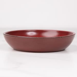 May include: A small, round, red ceramic bowl. The bowl is smooth and has a slight gloss.