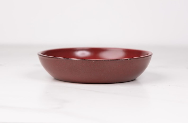 May include: A small, round, red ceramic bowl. The bowl is smooth and has a slight gloss.
