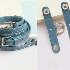 May include: A light blue leather strap with silver hardware, including a buckle and two adjustable strap keepers. The strap is coiled and laid flat on a white surface.