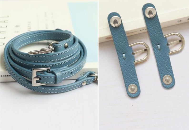 May include: A light blue leather strap with silver hardware, including a buckle and two adjustable strap keepers. The strap is coiled and laid flat on a white surface.