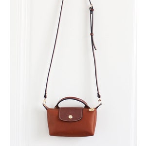 May include: A brown leather and nylon crossbody bag with a gold-toned clasp and a long adjustable strap.