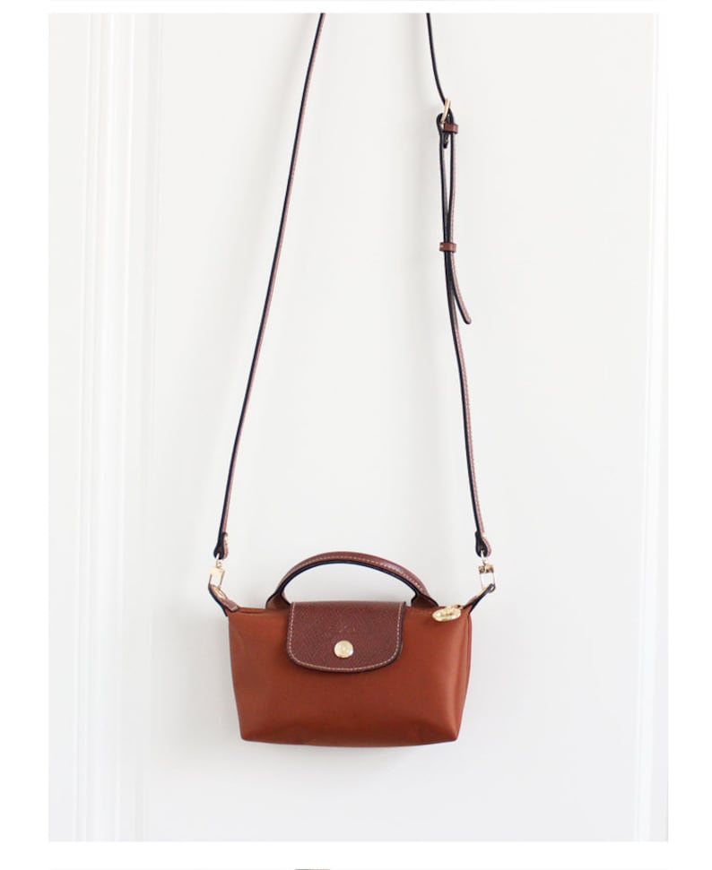 May include: A brown leather and nylon crossbody bag with a gold-toned clasp and a long adjustable strap.