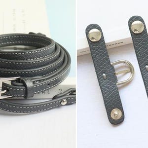 May include: A gray leather camera strap with a silver buckle and two adjustable straps with silver buckles.