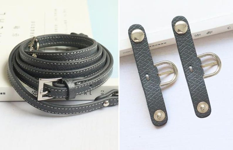 May include: A gray leather camera strap with a silver buckle and two adjustable straps with silver buckles.