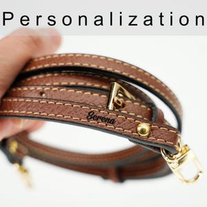 May include: Brown leather strap with a gold buckle and a personalized inscription that reads "Serena".