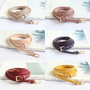 May include: Five different coloured leather straps with gold buckles and hardware. The straps are all the same length and width, and they are all coiled up. The straps are in the colours pink, beige, purple, red, and yellow.