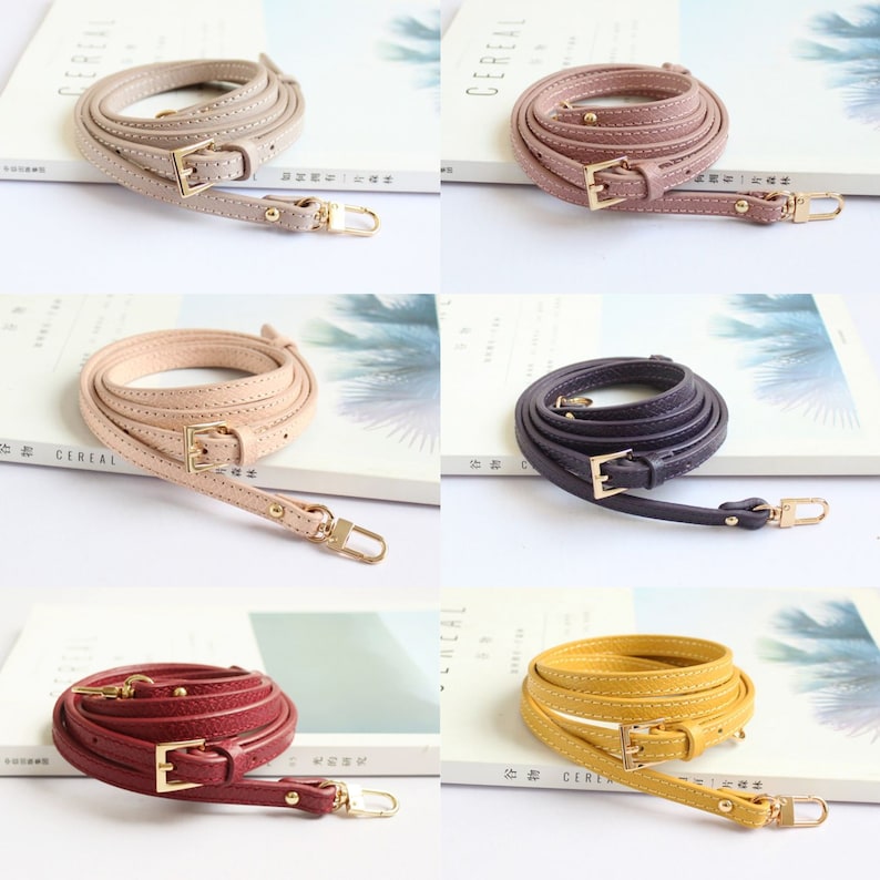 May include: Five different coloured leather straps with gold buckles and hardware. The straps are all the same length and width, and they are all coiled up. The straps are in the colours pink, beige, purple, red, and yellow.