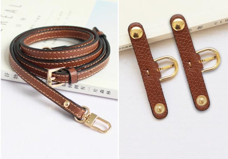 May include: A brown leather strap with gold hardware, including a buckle and two adjustable strap extenders. The strap is designed for a bag or purse.