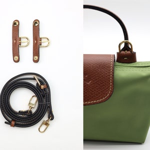 May include: A green nylon handbag with brown leather trim and a gold-tone zipper. The bag comes with a black adjustable shoulder strap and two brown leather strap attachments.