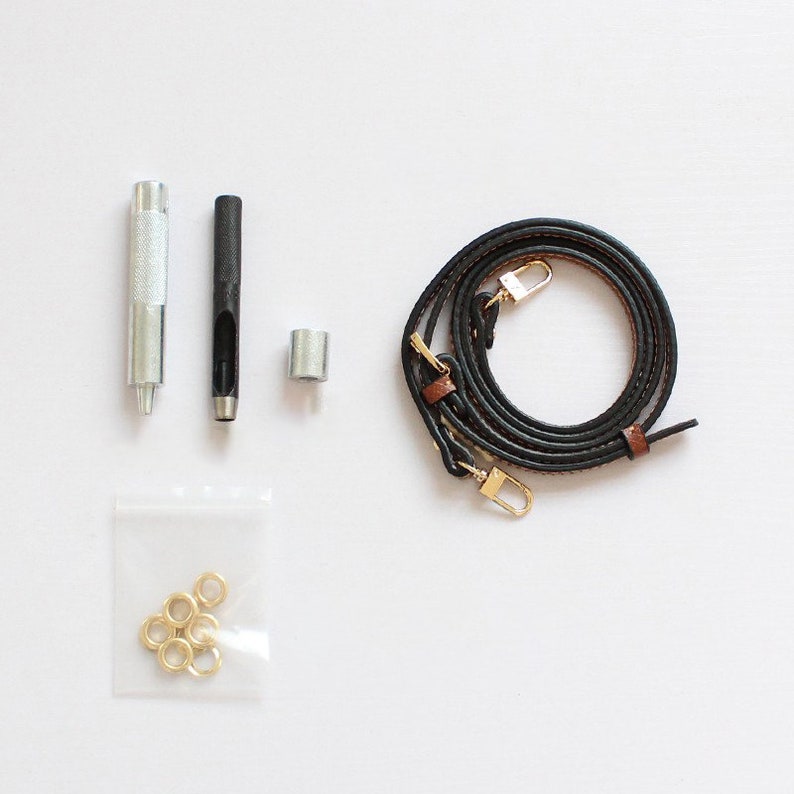 May include: A set of leather crafting tools and supplies including a black leather strap, two metal hole punches, a metal grommet, and a bag of gold metal grommets.