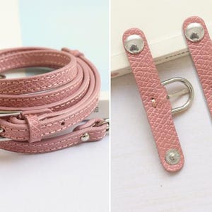 May include: A pink leather strap with a silver buckle and two silver snap closures. The strap is coiled and the closures are shown separately.