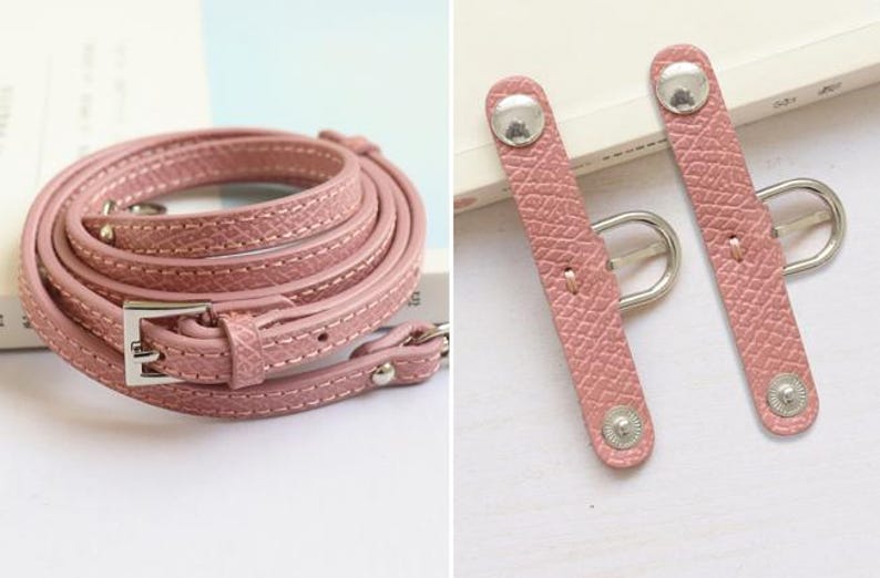 May include: A pink leather strap with a silver buckle and two silver snap closures. The strap is coiled and the closures are shown separately.