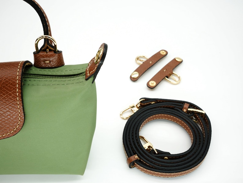 May include: A green nylon handbag with brown leather trim and a gold-tone zipper. The bag comes with a black and brown adjustable shoulder strap and two brown leather strap connectors.