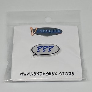 May include: A pin badge with a speech bubble design containing three blue question marks. The pin is on a white card with the text "WWW.VENDAGEEK.STORE" and a logo. The pin is packaged in a clear plastic bag.