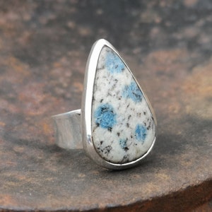 May include: A teardrop-shaped ring with a blue and white speckled stone set in a silver band.