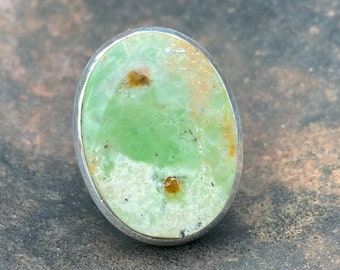 Könnte beinhalten: Ein ovaler Ring mit einem grünen und braunen Edelstein, der in Silber gefasst ist.
