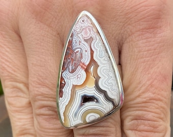 May include: A silver ring with a triangular shaped agate stone. The stone has a white, brown, and red banded pattern.