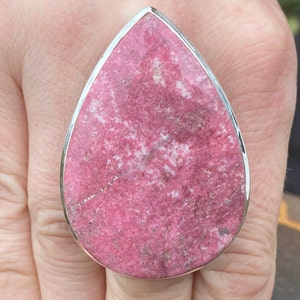 Peut inclure: Une bague en forme de larme avec une pierre précieuse rose et blanche sertie dans une bande argentée.