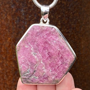 Peut inclure: Un pendentif en argent avec une grande pierre de rubis facetée rose. Le rubis est serti dans une bélière en argent et a une forme hexagonale.