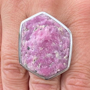 Könnte beinhalten: Ein silberner Ring mit einem großen, facettierten rosafarbenen Edelstein. Der Edelstein ist in einer sechseckigen Fassung gefasst.