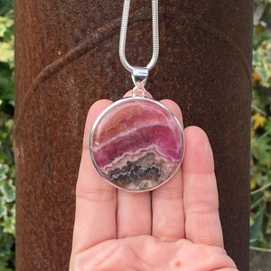 May include: A silver chain necklace with a round pendant featuring a pink and gray banded gemstone.