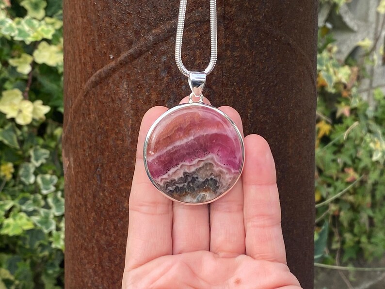 May include: A silver chain necklace with a round pendant featuring a pink and gray banded gemstone.
