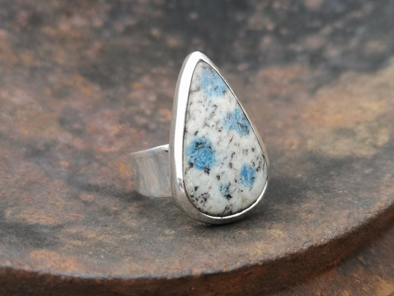 May include: A teardrop-shaped ring with a blue and white speckled stone set in a silver band.
