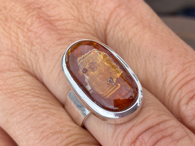 May include: A silver ring with an oval-shaped amber stone. The stone has a unique pattern of inclusions, giving it a distinctive look.