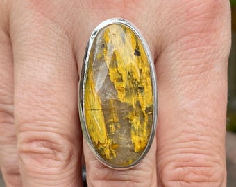 May include: Silver ring with an oval gemstone. The stone displays a pattern of yellow and gold colours, with a clear centre. The ring is a statement piece, suitable for adding a touch of elegance. The ring is a statement piece, suitable for adding a touch of elegance.