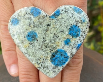 May include: A heart-shaped ring made of silver with a blue and white speckled stone.