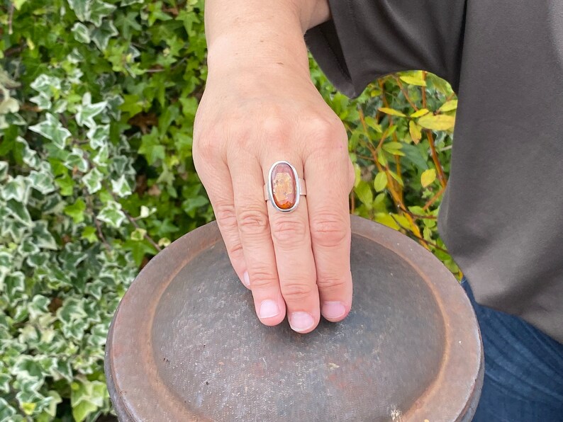May include: A silver ring with an oval-shaped amber stone set in a silver bezel. The ring is on a person's finger.