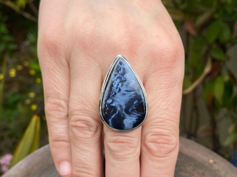 May include: A large, teardrop-shaped ring featuring a polished blue and white stone set in a silver-colored metal band. The stone has a swirling pattern, and the ring is displayed on a hand.