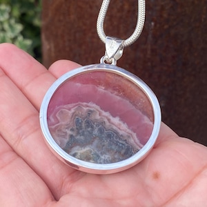 May include: A silver pendant necklace with a round pink and gray stone set in a silver bezel.