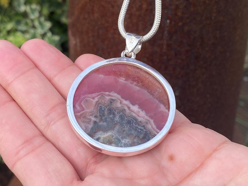 May include: A silver pendant necklace with a round pink and gray stone set in a silver bezel.