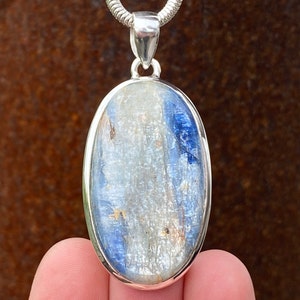 May include: A silver oval pendant featuring a blue and white gemstone. The gemstone has a striated pattern and a shimmering finish.