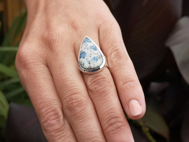 May include: A silver ring with a teardrop-shaped blue and white gemstone. The ring is on a person's finger.