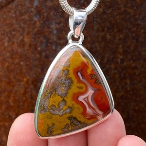 May include: A silver pendant featuring a triangular shaped agate stone with red, orange, yellow, and white swirling patterns.