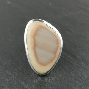 K&ouml;nnte beinhalten: Ein Silberring mit einem hellbraunen und wei&szlig;en Achat-Stein, der in der Mitte eingesetzt ist.