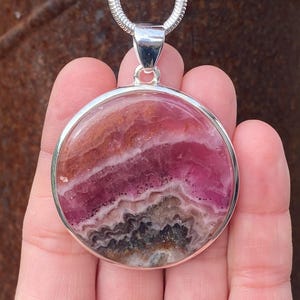 May include: A silver pendant featuring a round, pink and brown banded fluorite stone.