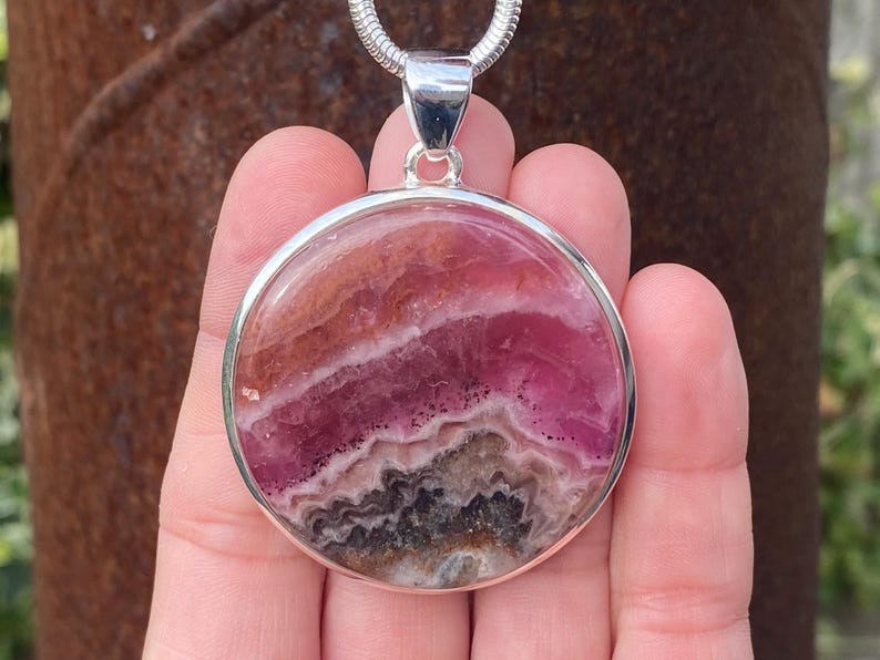 May include: A silver pendant featuring a round, pink and brown banded fluorite stone.