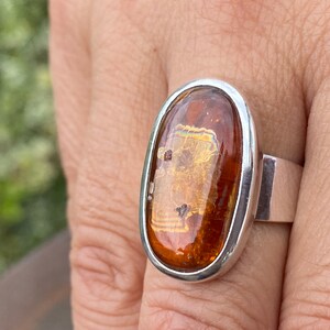 May include: A silver ring with an oval-shaped amber stone. The stone has a golden hue and is set in a silver bezel.