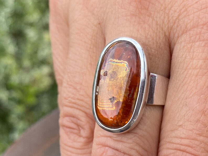May include: A silver ring with an oval-shaped amber stone. The stone has a golden hue and is set in a silver bezel.
