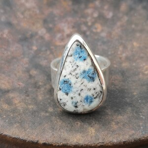 May include: A silver ring with a teardrop-shaped blue and white gemstone. The gemstone has a speckled pattern.