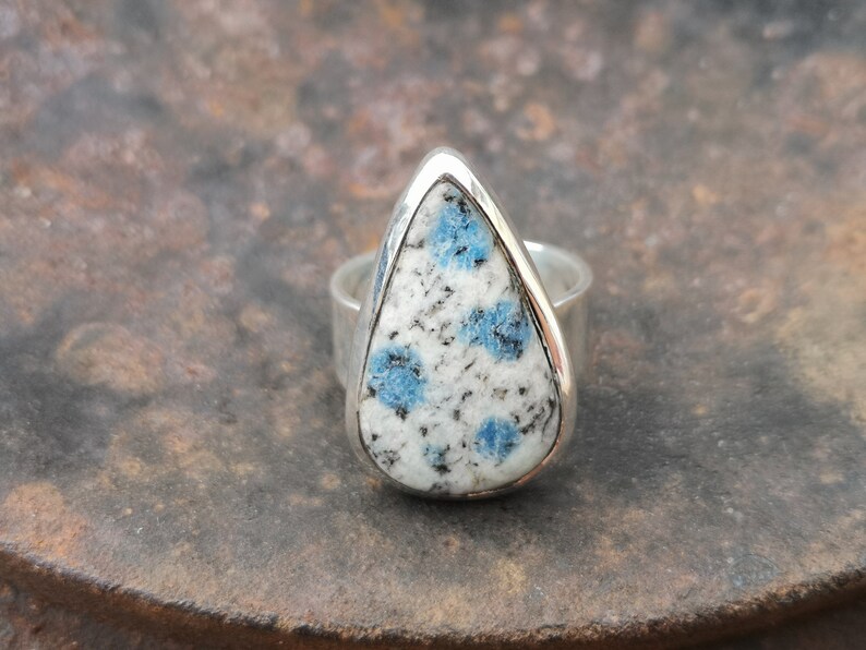 May include: A silver ring with a teardrop-shaped blue and white gemstone. The gemstone has a speckled pattern.