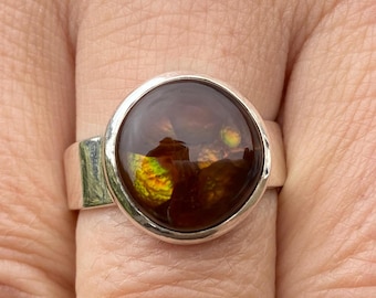 May include: A silver ring with a round, brown agate gemstone set in a bezel setting. The agate has a swirling pattern of brown, yellow, and green.