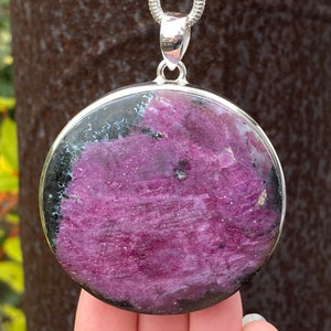May include: A round silver pendant featuring a pink and black gemstone. The gemstone has a rough, textured surface.