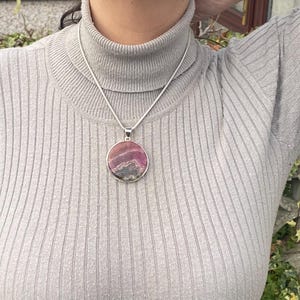May include: A silver chain necklace with a round pendant featuring a pink and gray patterned stone.