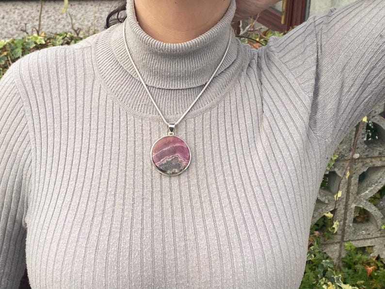 May include: A silver chain necklace with a round pendant featuring a pink and gray patterned stone.