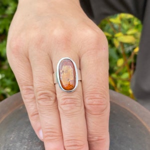May include: A silver ring with an oval-shaped amber stone. The stone has a translucent, golden-brown color with flecks of white.