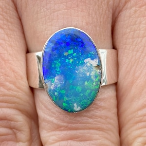 Könnte beinhalten: Ein silberner Ring mit einem großen ovalen blauen Opal-Edelstein. Der Opal hat ein blaues, grünes und weißes Farbmuster.